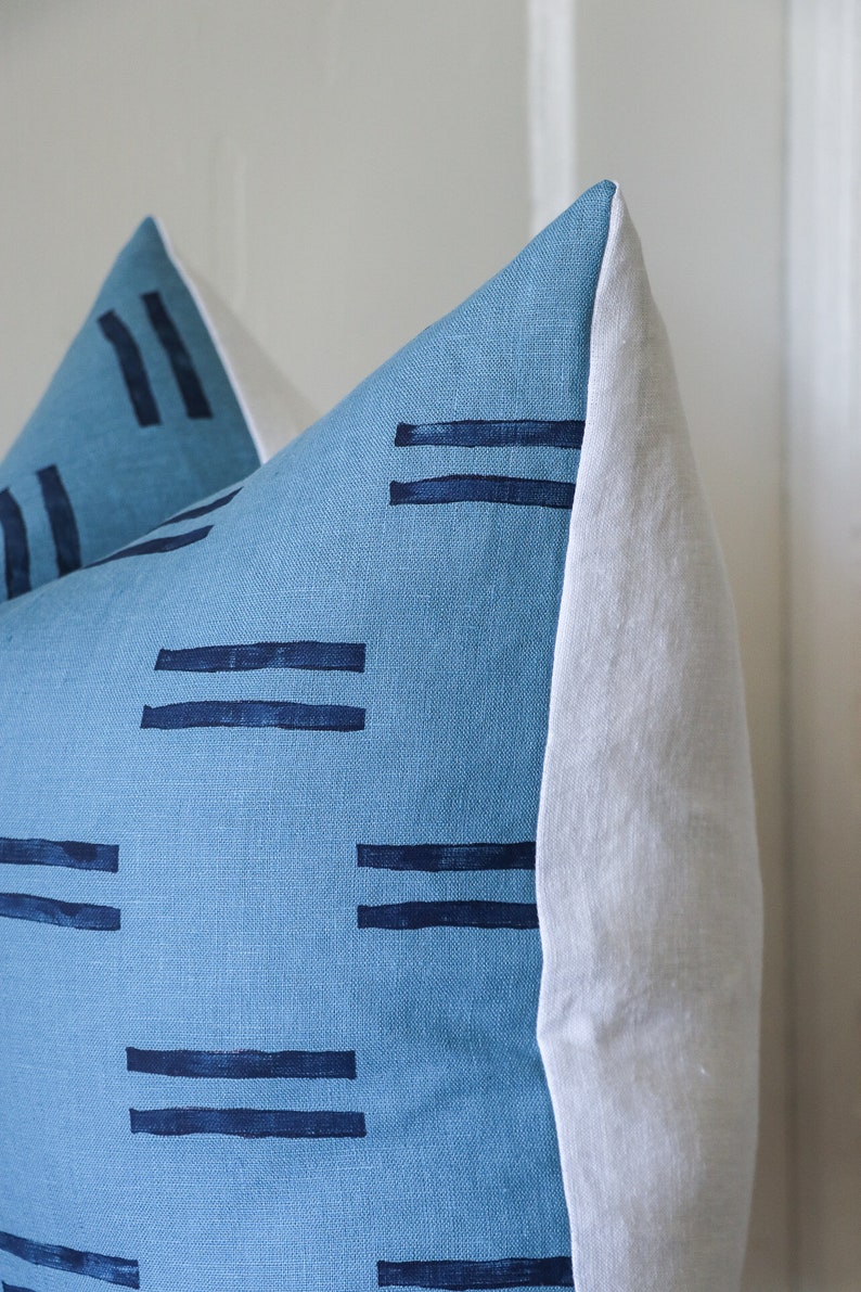 Puede incluir: Una almohada azul y blanca con un patr&oacute;n geom&eacute;trico de l&iacute;neas dobles. La almohada est&aacute; hecha de una tela suave y texturizada.