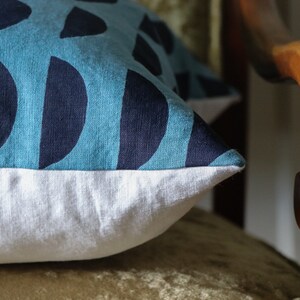 May include: A blue and white patterned throw pillow with a white border. The pillow is sitting on a wooden chair.