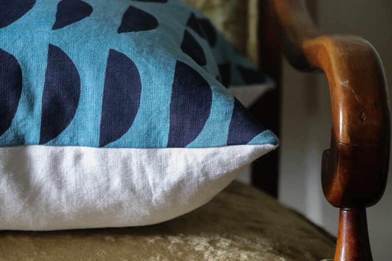 May include: A blue and white patterned throw pillow with a white border. The pillow is sitting on a wooden chair.