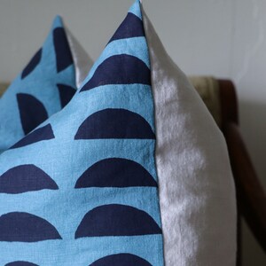 May include: A blue and navy blue pillow with a geometric pattern of half circles. The pillow is made of a soft, textured fabric.