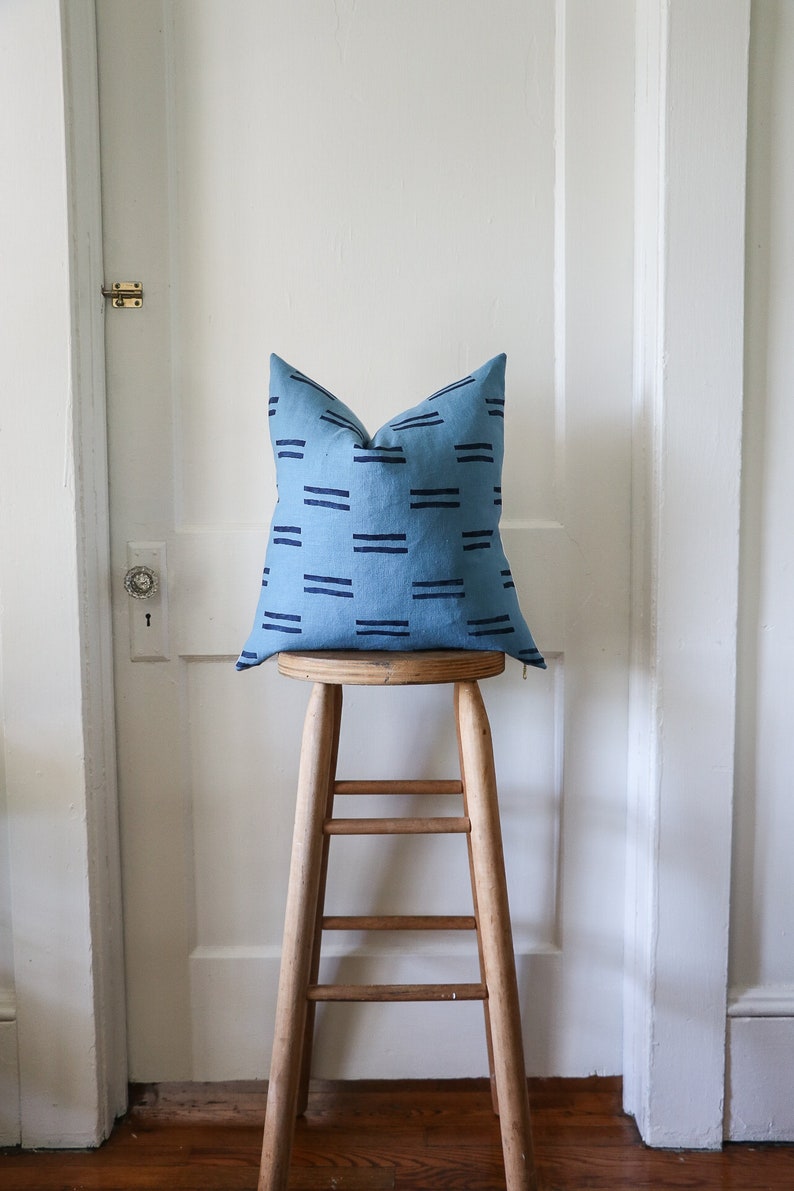 Puede incluir: Una almohada azul y negra con estampado se encuentra sobre un taburete de madera. La almohada est&aacute; hecha de una tela suave y texturizada y tiene un dise&ntilde;o geom&eacute;trico simple.