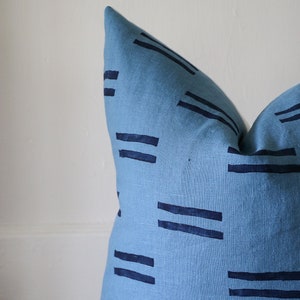 Puede incluir: Una almohada azul con un patr&oacute;n geom&eacute;trico de l&iacute;neas azul oscuro. La almohada est&aacute; hecha de una tela suave y texturizada.