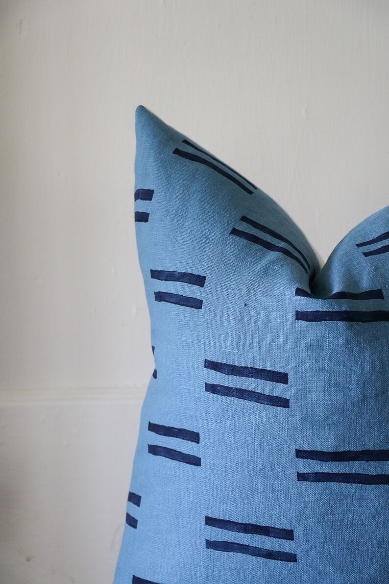 Puede incluir: Una almohada azul con un patr&oacute;n geom&eacute;trico de l&iacute;neas azul oscuro. La almohada est&aacute; hecha de una tela suave y texturizada.