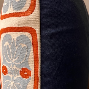 May include: Close-up of a decorative pillow with a navy blue side and a patterned side. The patterned side features a light blue floral design with orange accents on an off-white background. The pillow has a textured appearance.