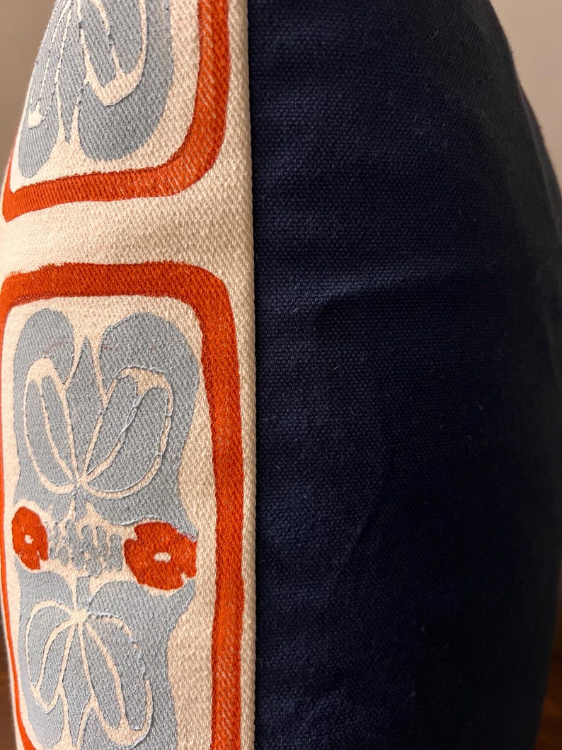 May include: Close-up of a decorative pillow with a navy blue side and a patterned side. The patterned side features a light blue floral design with orange accents on an off-white background. The pillow has a textured appearance.