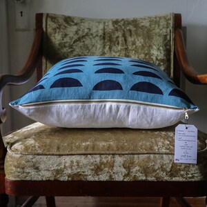 May include: A blue and navy blue patterned pillow with a white zipper and a white tag attached. The pillow is sitting on a green velvet chair.