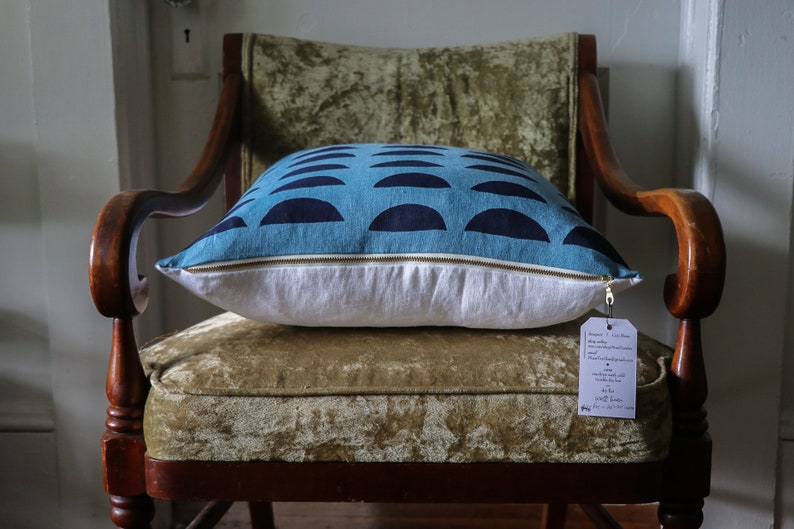 May include: A blue and navy blue patterned pillow with a white zipper and a white tag attached. The pillow is sitting on a green velvet chair.