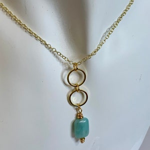 May include: A gold chain necklace with a pendant featuring two interlocking gold rings and a light blue square gemstone.