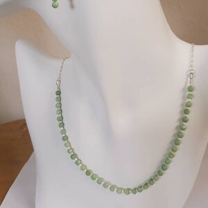 May include: A silver necklace and earrings set with light green beads. The necklace is a simple chain with green beads evenly spaced along the length. The earrings are drop earrings with two green beads on each earring.
