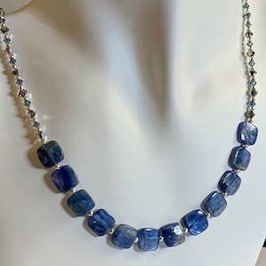 May include: A silver chain necklace with blue gemstone beads. The beads are square shaped and have a light blue and dark blue color.