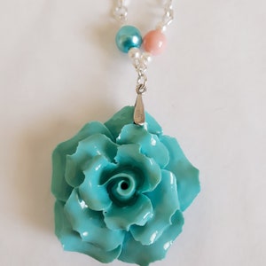 K&ouml;nnte beinhalten: Eine Halskette mit einem Anh&auml;nger in Form einer t&uuml;rkisblauen Rose, einer silbernen Kette und rosa und blauen Perlenakzenten.