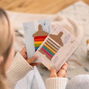 Peut inclure: Deux cartes avec du fil à broder coloré enroulé autour de formes d'avions en carton. Les cartes sont étiquetées "Rainbow Threads" et "Electric Threads".