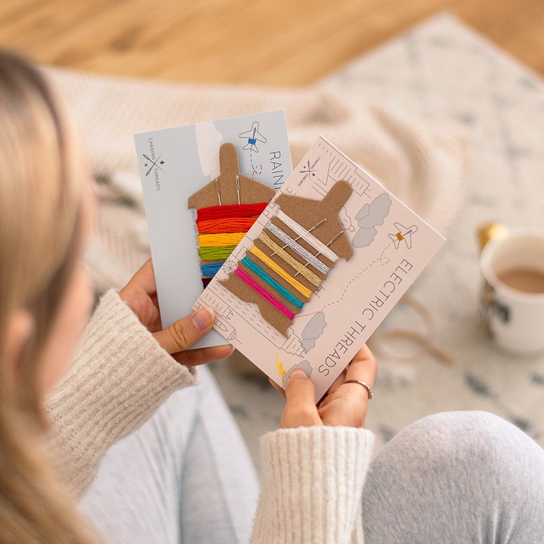 May include: Two cards with colourful embroidery floss wound around cardboard airplane shapes. The cards are labelled "Rainbow Threads" and "Electric Threads".