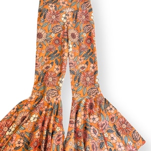 May include: Orange bell-bottom pants with a floral pattern in shades of pink, peach, and white. The pants have a high waist and a wide flare from the knee down. The floral design includes various flower types and green leaves.