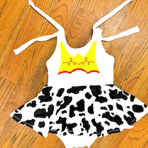 May include: White sleeveless dress with a yellow and red cowgirl vest design and a black and white cow print skirt.