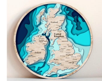 May include: A wooden map of the United Kingdom with a layered, 3D effect. The map is painted in shades of blue and features the names of major cities and regions, including Scotland, England, Wales, Northern Ireland, and Ireland.