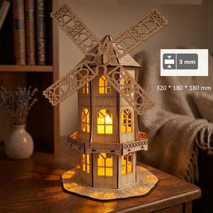 Peut inclure: Maquette de moulin à vent en bois avec des détails découpés complexes. Le modèle est éclairé de l'intérieur, mettant en valeur les fenêtres. Dimensions : 320 x 180 x 180 mm, épaisseur 3 mm. Les pales sont visibles. Posé sur une base en bois.