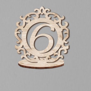 May include: Wooden table number holder with a decorative design and the number 6.