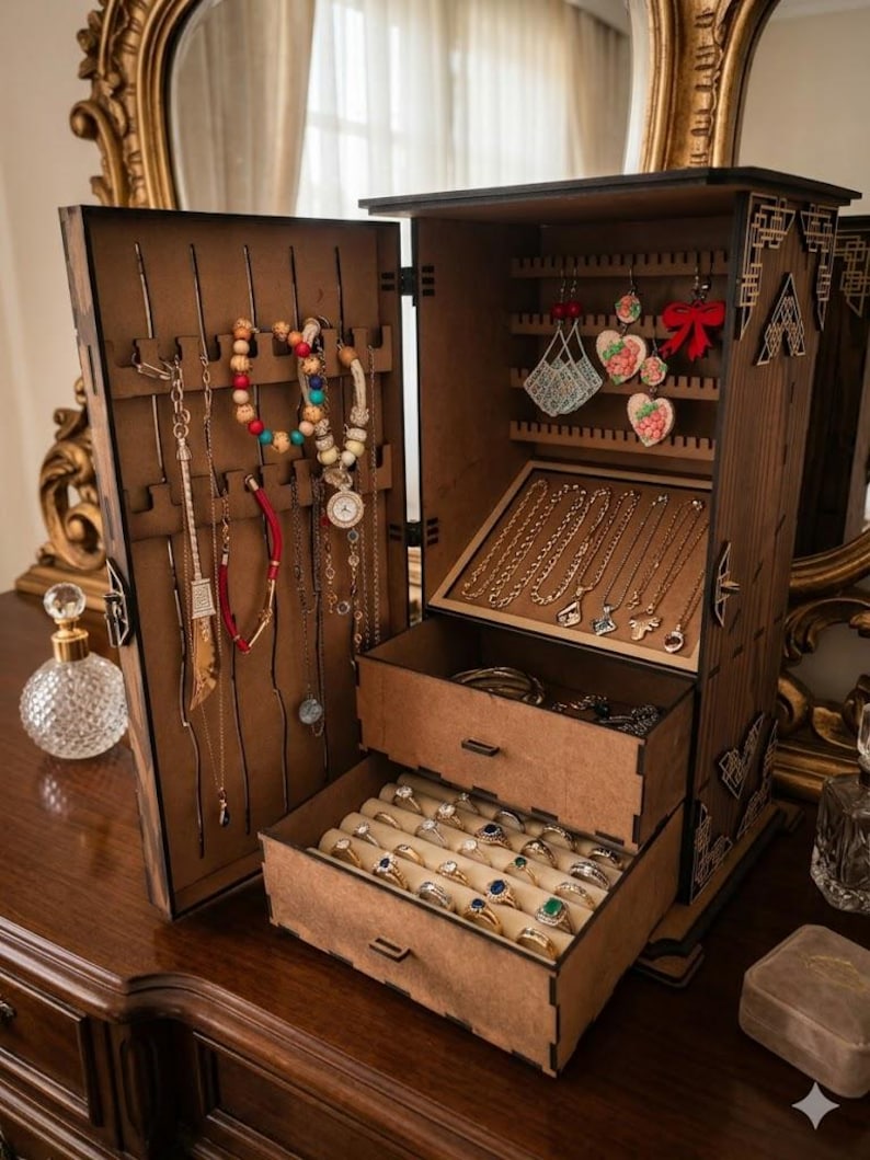 May include: A wooden jewelry armoire with multiple compartments and drawers. The open armoire displays necklaces, bracelets, earrings, and rings. The interior is lined with beige fabric. The armoire is on a wooden dresser.