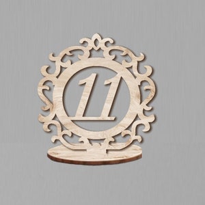 May include: Wooden table number holder with an ornate design and the number 11 in the center.