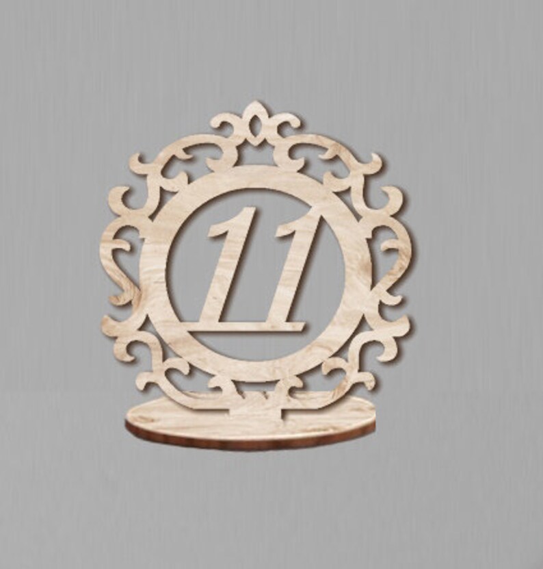 May include: Wooden table number holder with an ornate design and the number 11 in the center.