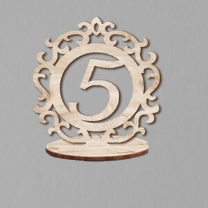 May include: Wooden table number holder with a decorative design and the number 5.