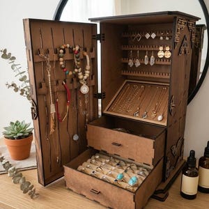 May include: A wooden jewelry armoire with multiple compartments and drawers. The open armoire displays necklaces, earrings, bracelets, and rings. The wood has a warm brown tone, and the interior is lined with beige fabric.