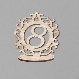 May include: Wooden table number holder with an ornate frame and the number 8 in the center.