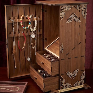 May include: A wooden jewelry armoire with a hinged door and two drawers. The armoire is made of dark wood and features decorative geometric cutouts. Various necklaces and bracelets hang inside. A small tray with a gold necklace is in front.