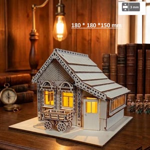 May include: A wooden model house featuring a gabled roof, decorative trim, and a small cart in front. The structure has illuminated windows and measures 180 x 180 x 150 mm with 3 mm thick components. The model is set on a flat base.