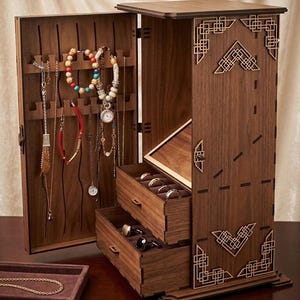 May include: A wooden jewelry box with an open door displaying necklaces and bracelets. The box has two drawers and a small tray. The box is brown with decorative geometric cutouts. The jewelry box is on a dark brown surface.