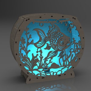 May include: A wooden cutout of a fish tank with a blue light shining through the cutout of a fish and plants. The fish tank is made of wood and has a round shape.