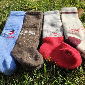 Op de afbeelding: Vier paar kleurrijke sokken met verschillende winterthema-ontwerpen. De sokken zijn gemaakt van een zachte, gebreide stof en hebben verschillende kleuren, waaronder blauw, bruin, rood en wit.