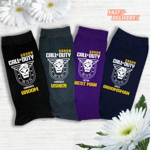 Könnte beinhalten: Vier Paar Socken in Schwarz, Grau, Lila und Marineblau. Jede Socke hat eine weiße Grafik mit einem Totenkopf und dem Text "Groom Call of Duty" sowie eine Rolle wie "Groom" oder "Best Man".