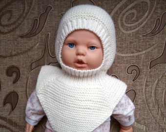 May include: A white knitted baby hat and neck warmer set. The hat has a pointed top and covers the ears. The neck warmer is a cowl style and covers the neck and shoulders.
