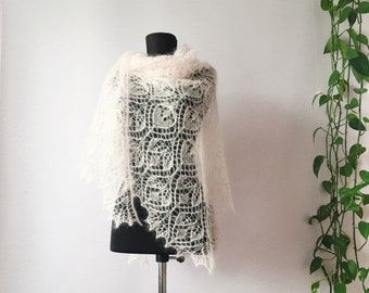 Puede incluir: Un chal de encaje blanco con un delicado patrón floral, exhibido en un maniquí.