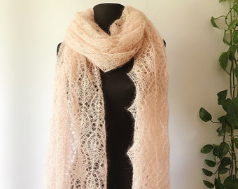 Puede incluir: Un chal de punto delicado de color rosa claro con un patrón de encaje. El chal está drapeado sobre un maniquí negro.