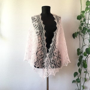 K&ouml;nnte beinhalten: Ein zartes, rosafarbenes gestricktes Tuch mit einem Spitzenmuster. Das Tuch ist &uuml;ber eine schwarze Schaufensterpuppe gelegt und hat einen gewellten Rand.