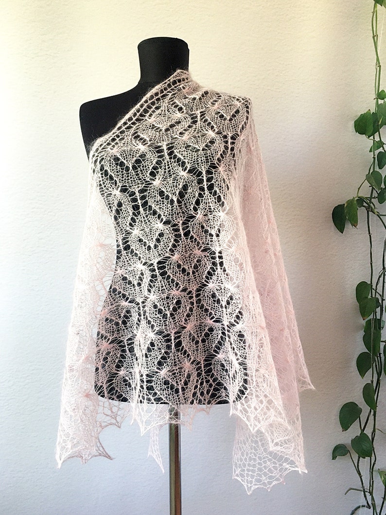 K&ouml;nnte beinhalten: Ein zartes, rosafarbenes gestricktes Tuch mit einem Spitzenmuster. Das Tuch ist &uuml;ber eine schwarze Schaufensterpuppe gelegt.
