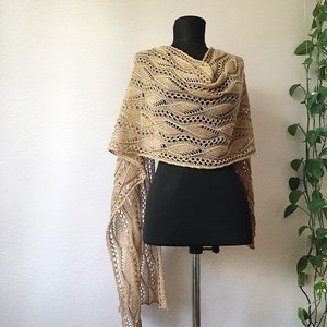 K&ouml;nnte beinhalten: Ein beigefarbener gestrickter Schal mit einem Spitzenmuster, der &uuml;ber eine schwarze Schaufensterpuppe gelegt wird.