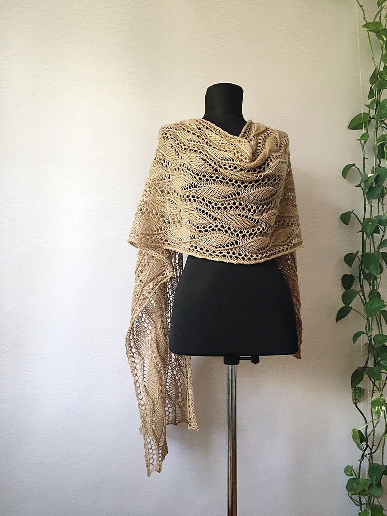 K&ouml;nnte beinhalten: Ein beigefarbener gestrickter Schal mit einem Spitzenmuster, der &uuml;ber eine schwarze Schaufensterpuppe gelegt wird.