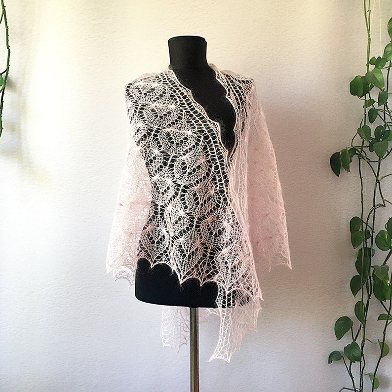 K&ouml;nnte beinhalten: Ein zartes, rosafarbenes gestricktes Tuch mit einem Spitzenmuster. Das Tuch ist &uuml;ber eine schwarze Schaufensterpuppe gelegt.