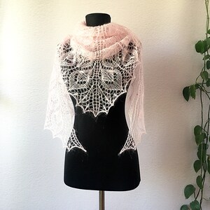 K&ouml;nnte beinhalten: Ein zartes, rosafarbenes gestricktes Tuch mit einem Spitzenmuster, das auf einer schwarzen Schaufensterpuppe pr&auml;sentiert wird.