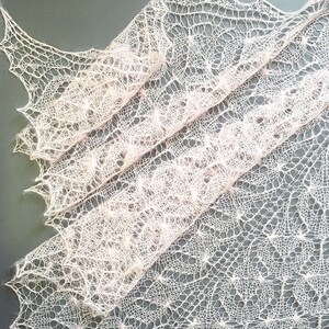K&ouml;nnte beinhalten: Ein zartes, handgestricktes Tuch in zartem Rosa. Das Tuch hat ein Spitzenmuster mit filigranen Mustern.