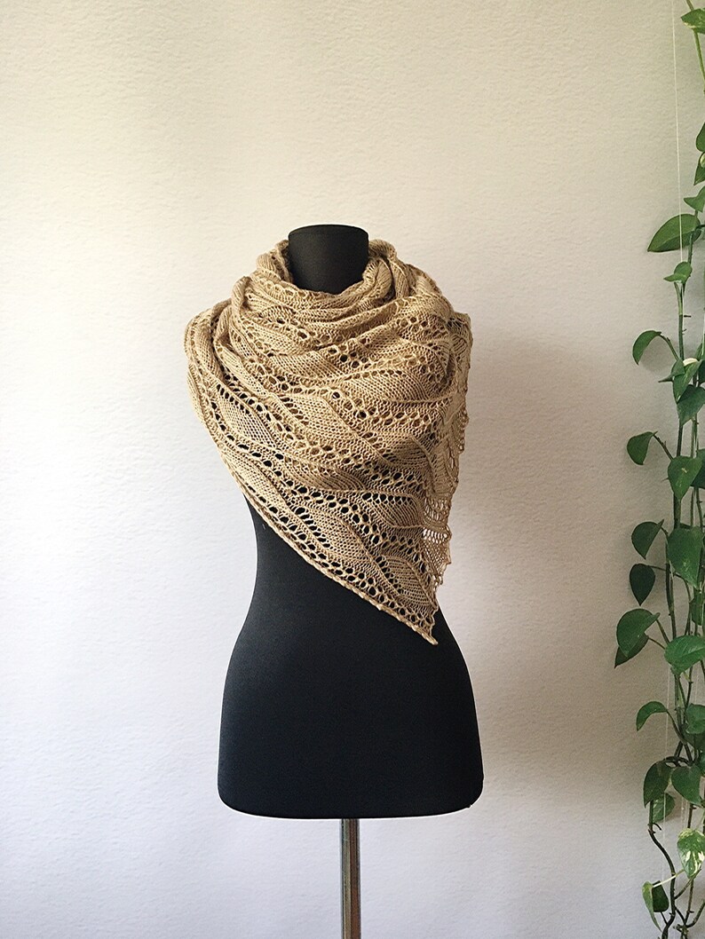 K&ouml;nnte beinhalten: Ein beigefarbener gestrickter Schal mit einem zarten Spitzenmuster, der &uuml;ber eine schwarze Schaufensterpuppe gelegt wird.