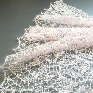 K&ouml;nnte beinhalten: Ein zartes, handgestricktes Tuch in zartem Rosa. Das Tuch ist mit einem Spitzenmuster gearbeitet und hat einen flie&szlig;enden, &auml;therischen Look.