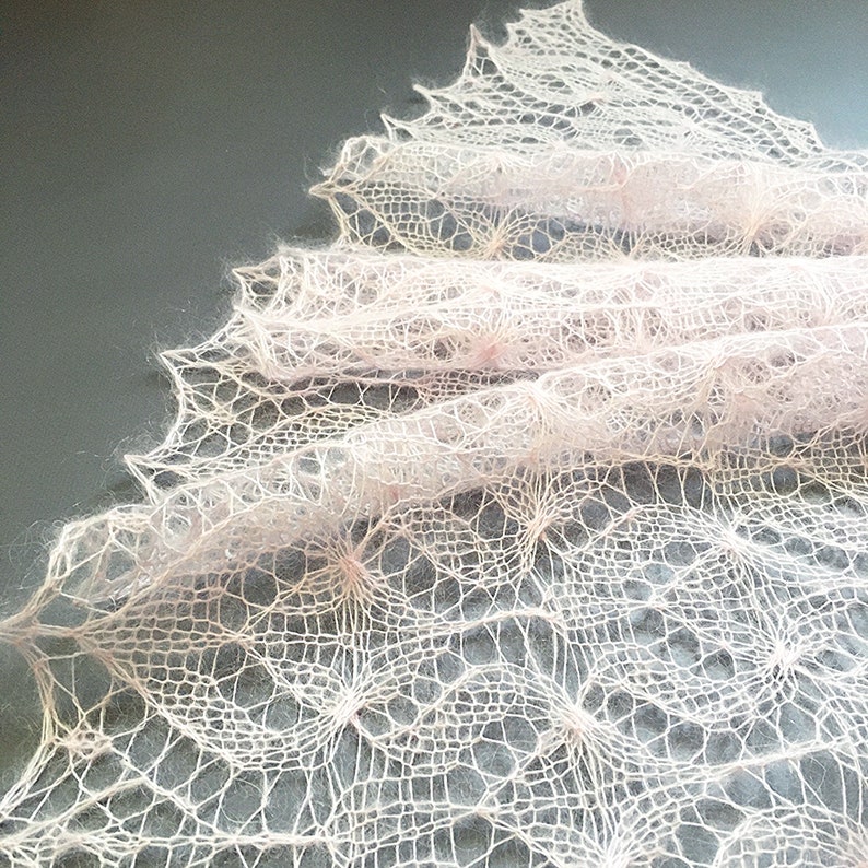 K&ouml;nnte beinhalten: Ein zartes, handgestricktes Tuch in zartem Rosa. Das Tuch ist mit einem Spitzenmuster gearbeitet und hat einen flie&szlig;enden, &auml;therischen Look.