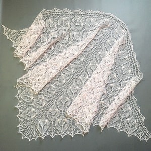 K&ouml;nnte beinhalten: Ein zartes, handgestricktes Tuch in einem sanften Rosa- und Wei&szlig;ton. Das Tuch ist aus feinem Garn gefertigt und hat ein zartes, durchbrochenes Muster.
