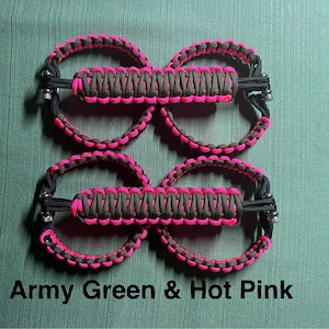 May include: Four sets of army green and hot pink paracord accessories. Each set features a central, rectangular section with a pink and green woven pattern, connected to two circular loops. The text "Army Green & Hot Pink" is at the bottom.