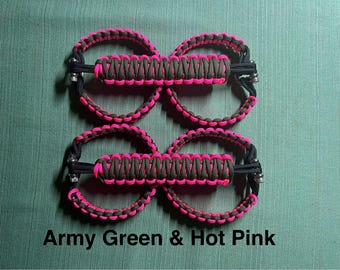May include: Four sets of army green and hot pink paracord accessories. Each set features a central, rectangular section with a pink and green woven pattern, connected to two circular loops. The text "Army Green & Hot Pink" is at the bottom.